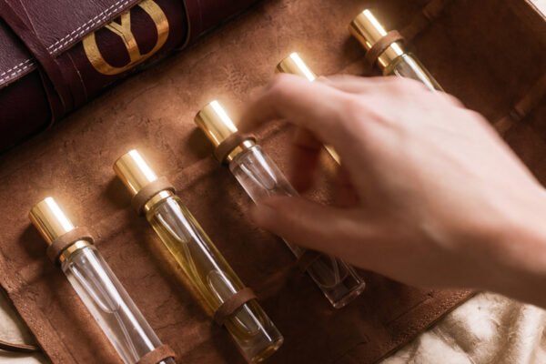 Elyamor Alchemist’s Love Potion custom perfume kit with five glass vials in a brown leather case on satin fabric, hand selecting a fragrance