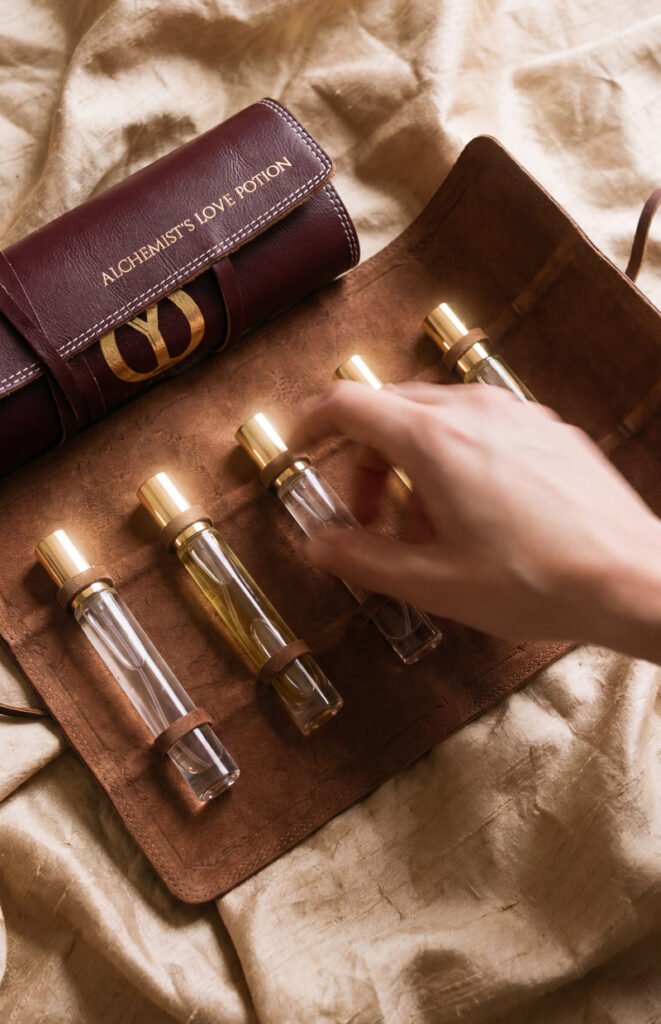 Elyamor Alchemist’s Love Potion custom perfume kit with five glass vials in a brown leather case on satin fabric, hand selecting a fragrance